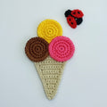 Crocheted ice cream cone patch with three scoops in brown, yellow, and pink, on a cream-colored waffle cone base, shown on a white background with a small ladybug embellishment.